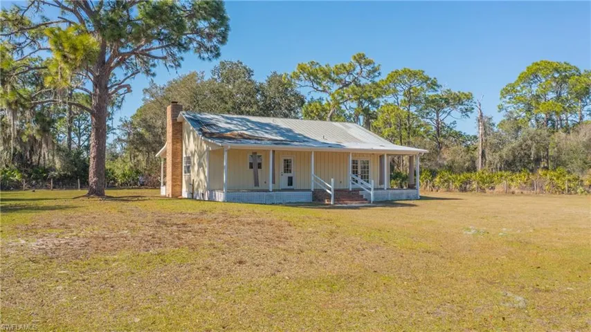 Farmhouse-style home featuring a front yard, a porch, a chimney, and view of scattered trees