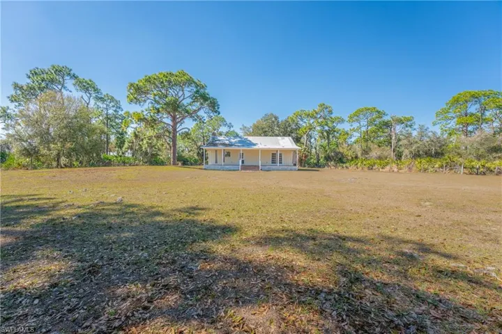 View of grassy yard with a porch and view of scattered trees
