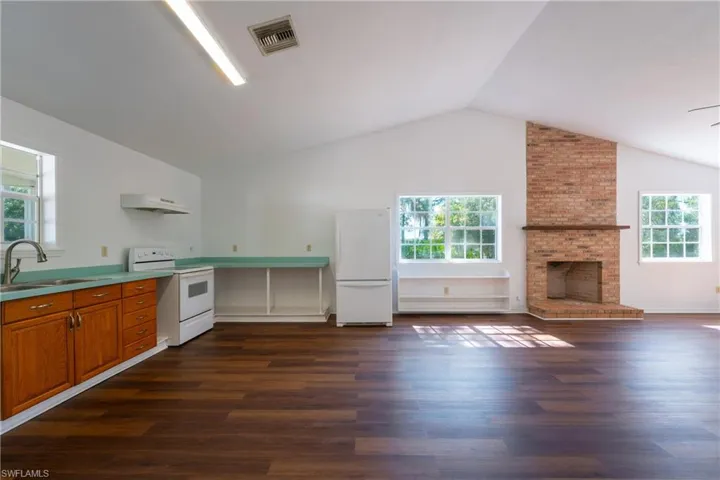 Kitchen featuring white appliances, wood finish cabinetry, light countertops, dark wood-style floors, and a brick fireplace