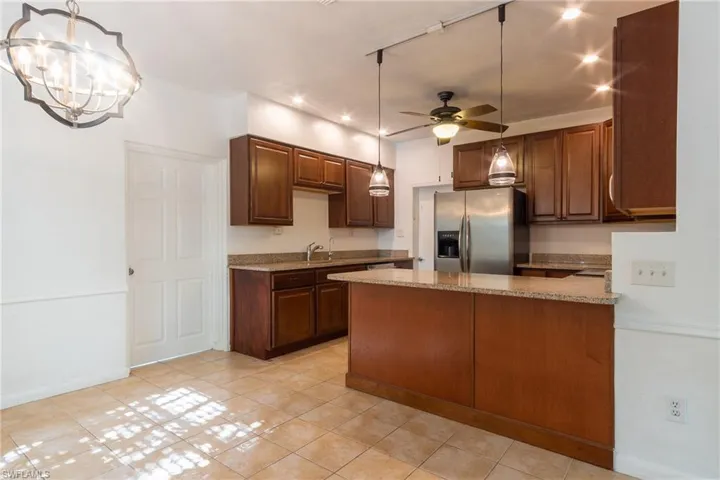 Kitchen with ceiling fan with notable chandelier, stainless steel fridge, light stone countertops, and hanging light fixtures