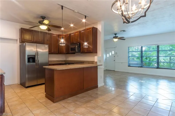 Kitchen with ceiling fan with notable chandelier, decorative light fixtures, stainless steel appliances, rail lighting, and light stone counters