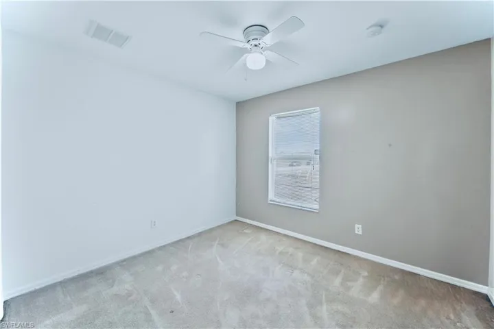 Empty room with carpet flooring, visible vents, baseboards, and ceiling fan