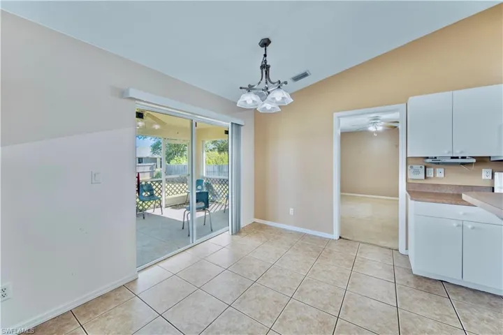Unfurnished dining area featuring ceiling fan with notable chandelier, light tile patterned floors, baseboards, and visible vents