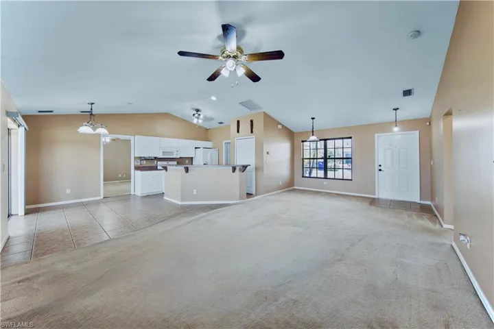Unfurnished living room featuring a ceiling fan, light carpet, lofted ceiling, and visible vents