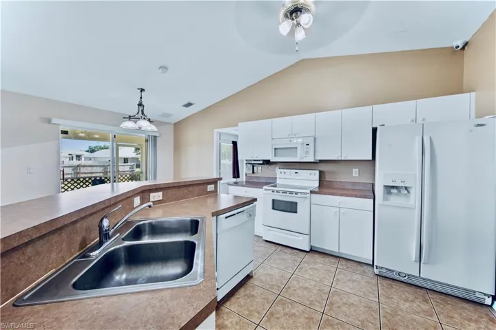 Kitchen with white appliances, a ceiling fan, white cabinetry, light tile patterned flooring, and a sink