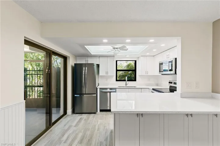Kitchen featuring stainless steel appliances, light wood finished floors, white cabinetry, a tray ceiling, and light stone counters