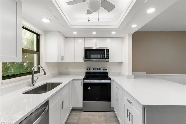 Kitchen with stainless steel appliances, light stone counters, a peninsula, white cabinets, and recessed lighting
