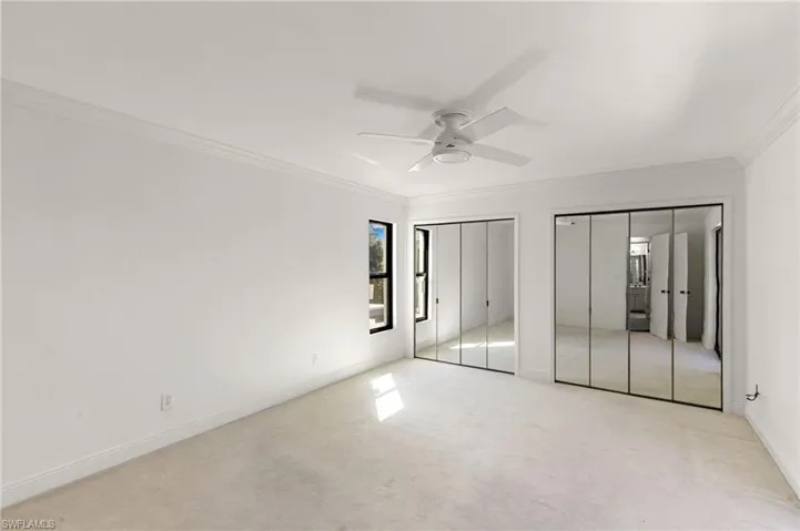 Unfurnished bedroom with two closets, carpet, crown molding, and ceiling fan