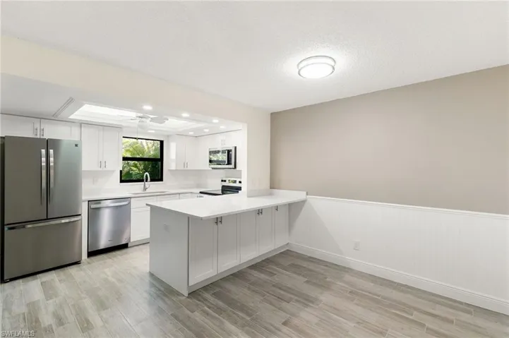 Kitchen with a wainscoted wall, stainless steel appliances, ceiling fan, white cabinetry, and a peninsula