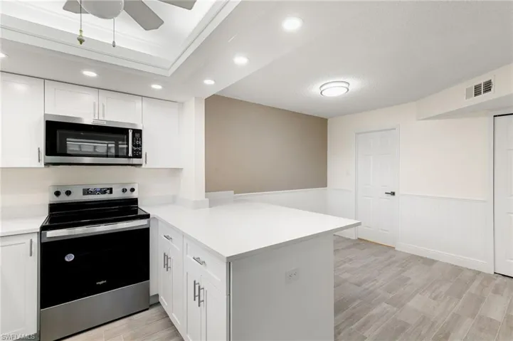 Kitchen with stainless steel appliances, wainscoting, a peninsula, light wood-style floors, and white cabinetry