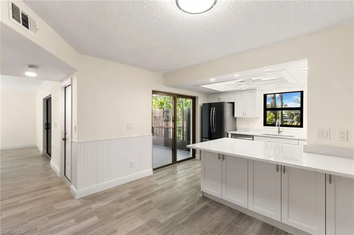 Kitchen with light wood-style floors, a peninsula, light stone countertops, wainscoting, and white cabinets