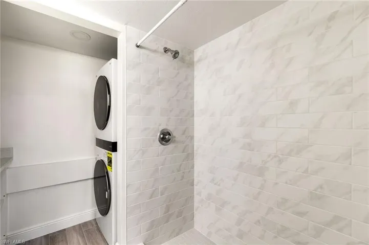 Bathroom featuring tiled shower, stacked washer / drying machine, and wood tiled floors
