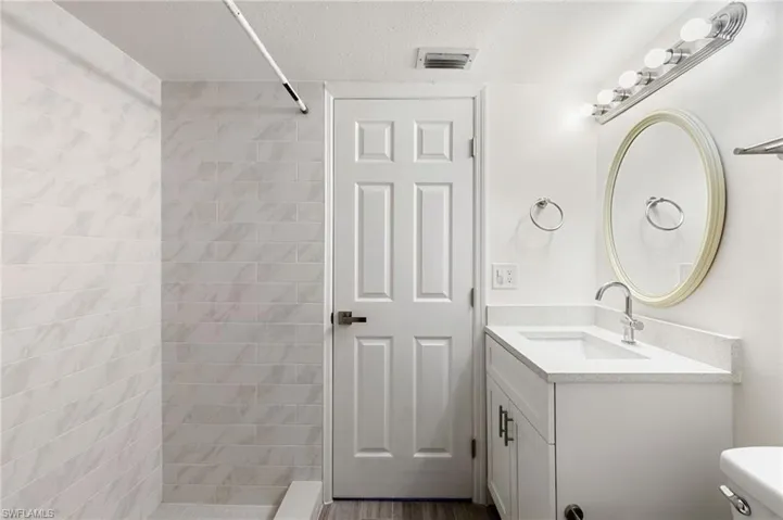 Bathroom with a textured ceiling, tiled shower, and vanity