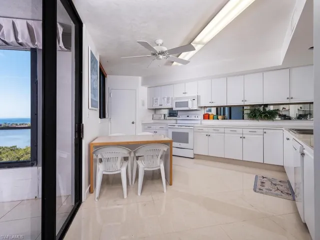 Kitchen featuring white cabinets, a kitchen bar, light tile patterned floors, ceiling fan, and white appliances