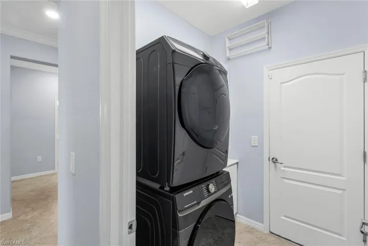 Laundry area featuring stacked washer / drying machine, light tile patterned floors, and crown molding