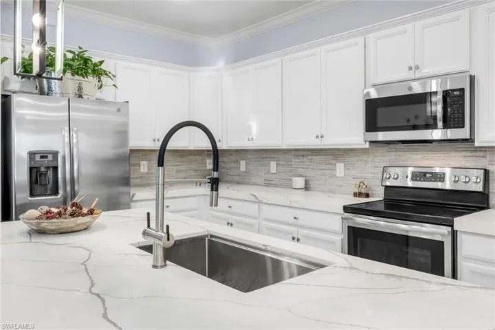 Kitchen with appliances with stainless steel finishes, tasteful backsplash, white cabinets, and crown molding