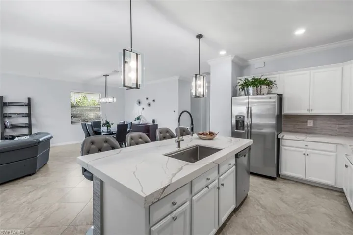 Kitchen featuring ornamental molding, white cabinets, backsplash, stainless steel appliances, and an island with sink