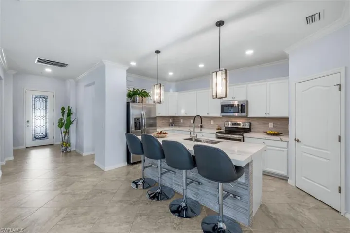 Kitchen featuring a kitchen breakfast bar, hanging light fixtures, tasteful backsplash, appliances with stainless steel finishes, and ornamental molding