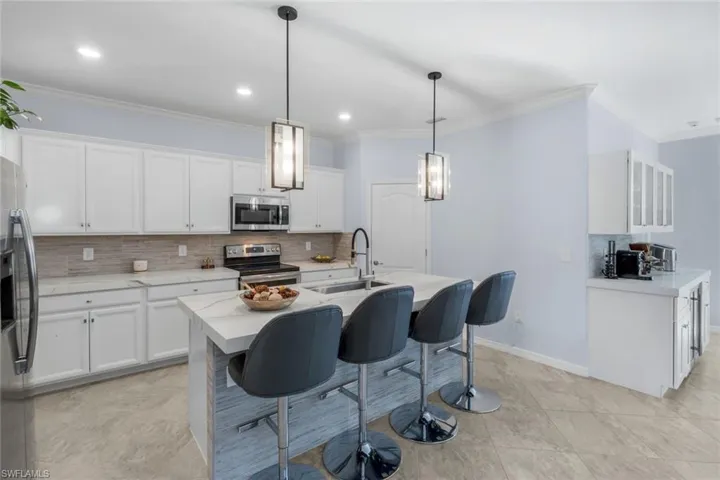 Kitchen with backsplash, a breakfast bar, white cabinetry, ornamental molding, and recessed lighting