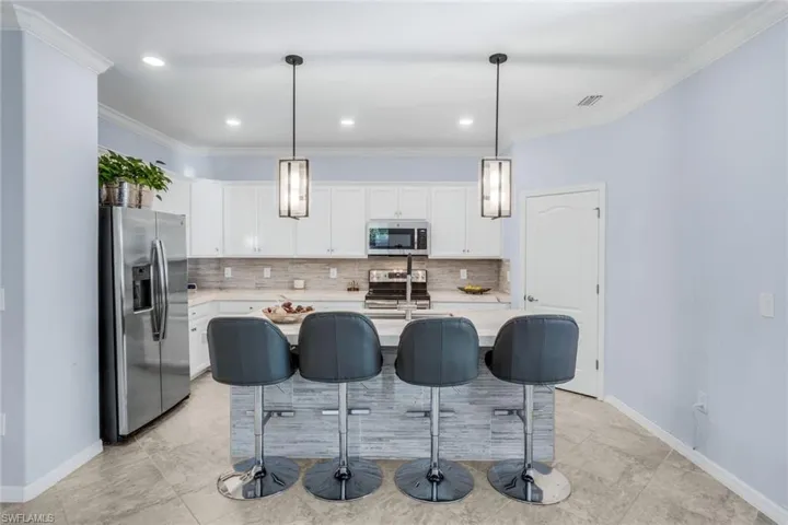 Kitchen with a breakfast bar area, stainless steel appliances, a kitchen island with sink, white cabinetry, and crown molding
