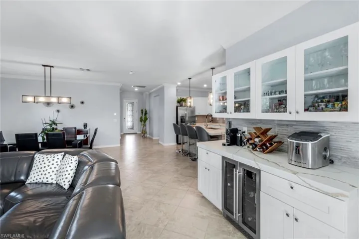 Bar area with tasteful backsplash, decorative light fixtures, white cabinetry, beverage cooler, and ornamental molding
