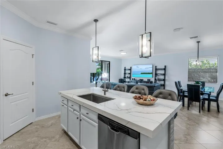 Kitchen with crown molding, an island with sink, pendant lighting, stainless steel dishwasher, and a chandelier