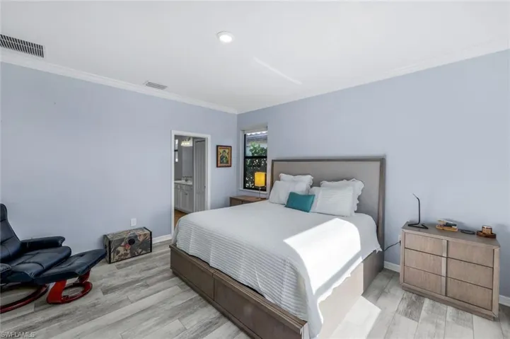Bedroom with ornamental molding, light wood-style flooring, and connected bathroom