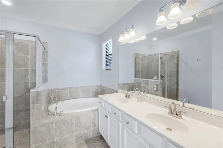 Bathroom with ornamental molding, a garden tub, a shower stall, double vanity, and recessed lighting