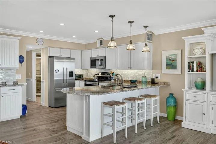 Kitchen with appliances with stainless steel finishes, a peninsula, white cabinets, light stone counters, and a kitchen breakfast bar