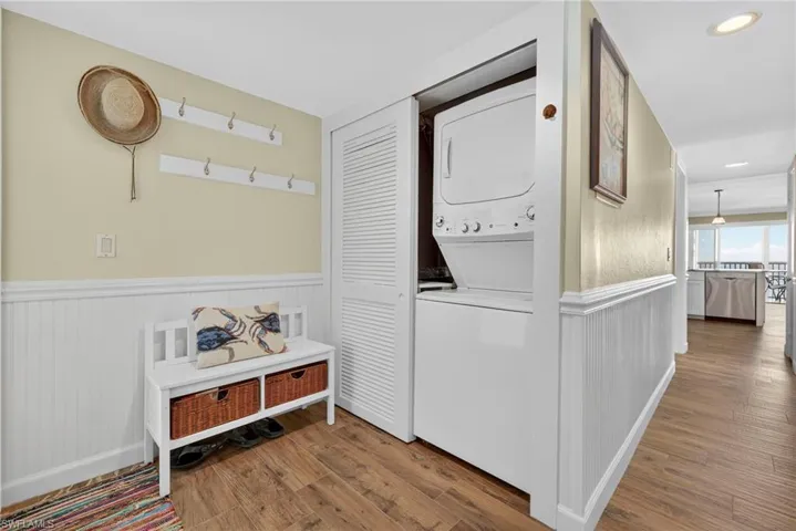 Laundry room featuring wood finished floors, stacked washer / dryer, and wainscoting
