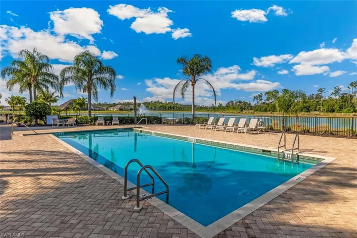 The property features an outdoor swimming pool surrounded by a paver deck, lounge chairs, and palm trees, with a lake and natural landscaping in the background
