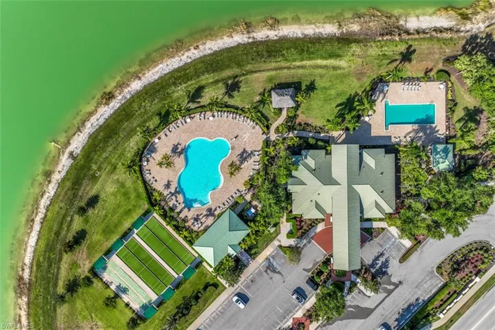 Aerial view showcasing the property's amenities, including two swimming pools, tennis courts, and a clubhouse, alongside a large body of water