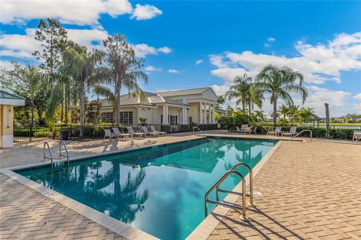 The property features a swimming pool with brick paver decking, surrounded by various palm trees and a manicured lawn