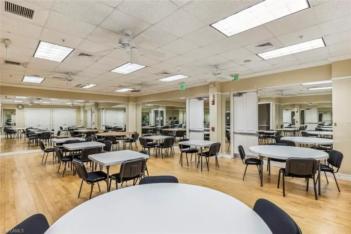 This spacious room features light wood flooring, a drop ceiling with recessed lighting and ceiling fans, and mirrored walls that enhance the sense of openness