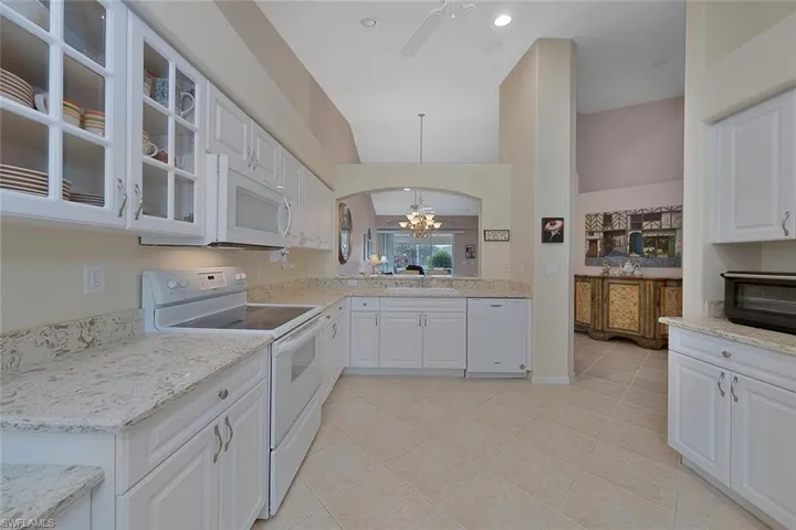 Kitchen with ceiling fan with notable chandelier, white appliances, white cabinets, and light tile patterned floors