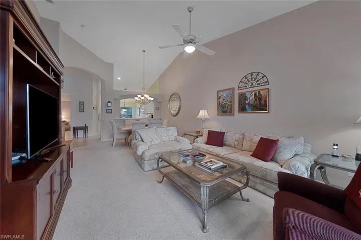 Living room featuring light carpet, high vaulted ceiling, and ceiling fan with notable chandelier