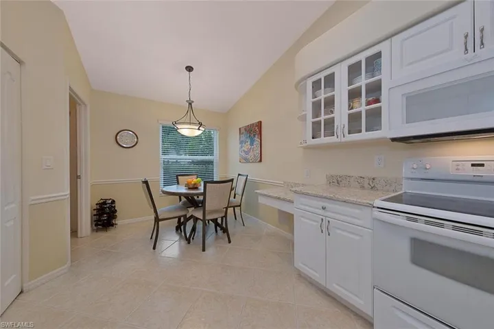 Kitchen featuring light tile patterned floors, light stone counters, white appliances, white cabinetry, and lofted ceiling