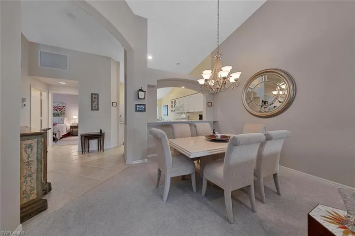 Dining space with light colored carpet, a notable chandelier, and high vaulted ceiling