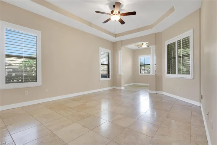 Empty room with a tray ceiling, ornate columns, a ceiling fan, and light tile patterned flooring