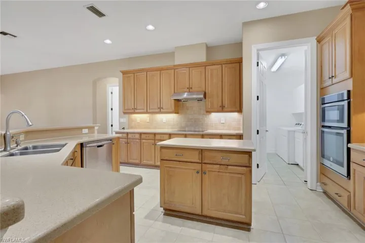 Kitchen with an island with sink, separate washer and dryer, appliances with stainless steel finishes, recessed lighting, and arched walkways