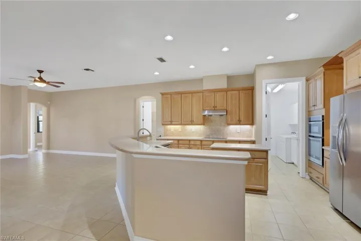 Kitchen with a kitchen island with sink, arched walkways, appliances with stainless steel finishes, light countertops, and backsplash