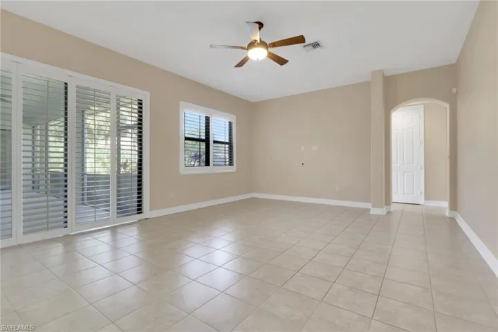 Empty room with ceiling fan, arched walkways, and light tile patterned floors