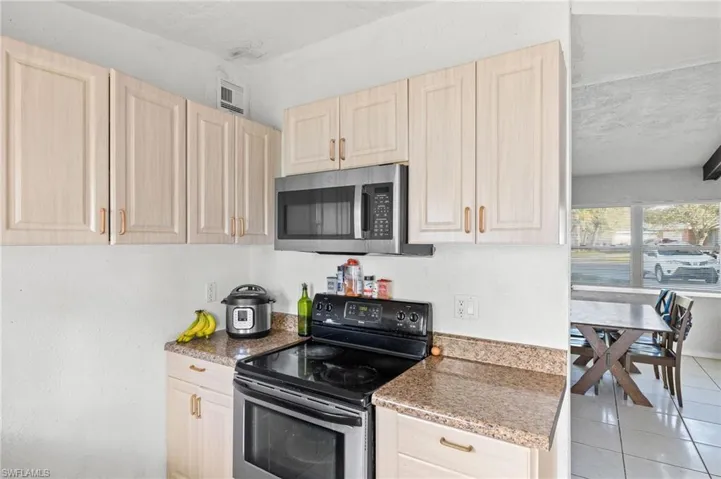 Kitchen featuring black electric range, light brown cabinetry, a textured ceiling, and light tile patterned flooring
