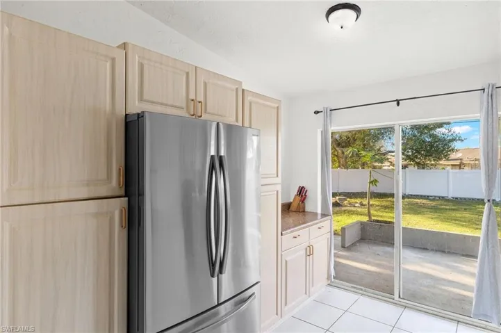 Kitchen featuring light tile patterned floors, light brown cabinetry, stainless steel refrigerator, and dark stone counters