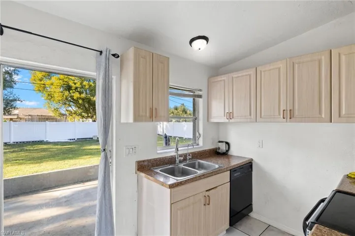 Kitchen with sink, lofted ceiling, black dishwasher, and light brown cabinetry