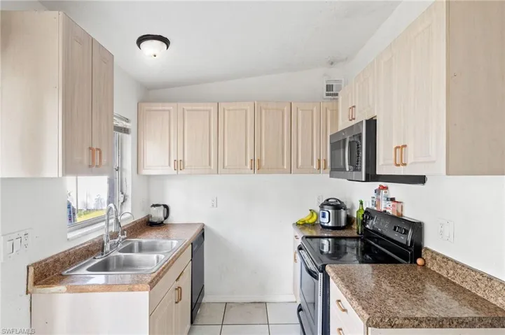 Kitchen featuring sink, light brown cabinets, lofted ceiling, light tile patterned flooring, and black appliances