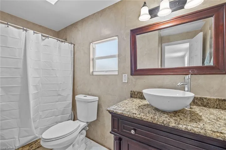 Bathroom featuring walk in shower, vanity, toilet, and tile walls