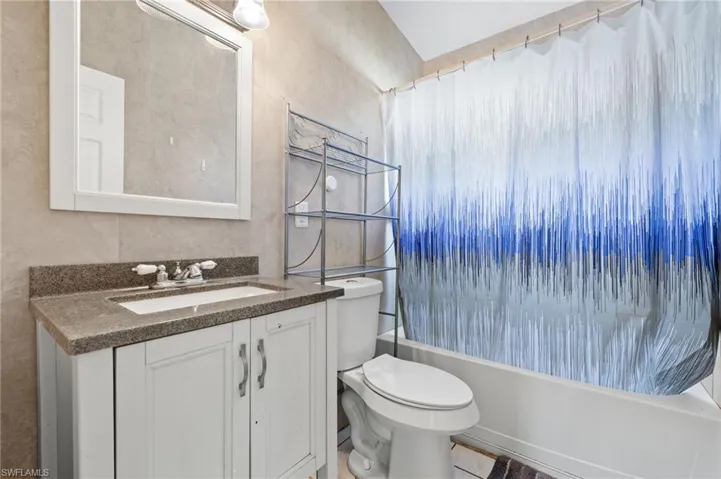 Full bathroom featuring vanity, shower / bath combination with curtain, toilet, and tile walls