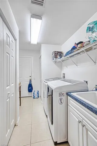 Laundry area with light tile patterned flooring, independent washer and dryer, and cabinet space