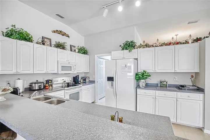 Kitchen featuring white appliances, white cabinetry, track lighting, a kitchen bar, and light tile patterned flooring